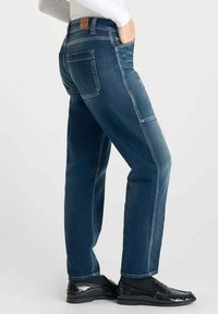 Jean en denim bleu avec une coupe droite, présentant des poches arrière et latérales, des coutures contrastées et une étiquette en cuir sur la ceinture.
