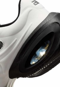 Zapatilla blanca con suela texturizada negra que presenta una cámara de aire transparente visible en el área del talón y ribete negro alrededor del tobillo.