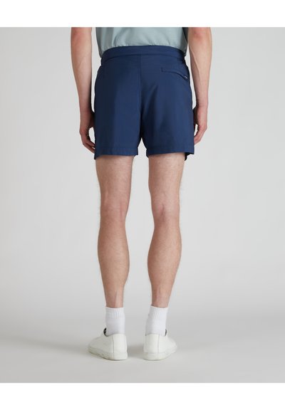 Marineblaue Shorts mit glatter Textur, elastischem Bund und einer einzelnen Gesäßtasche, kombiniert mit weißen Socken und Turnschuhen.