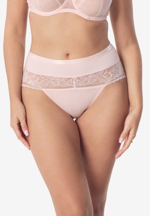 Kobieta w jasno różowych wysokich majtkach z koronkową lamówką oraz pasującym biustonoszu, stojąca na białym, jednolitym tle.