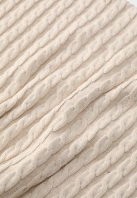 Couverture en tricot de couleur beige clair avec un motif de câble en relief. Texture douce avec une apparence chaude et confortable, adaptée à divers styles de décoration.