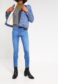 Denimjacka med faux-fur foder, i kombination med en grönrandig topp, blå smala jeans och svarta ankelstövlar.