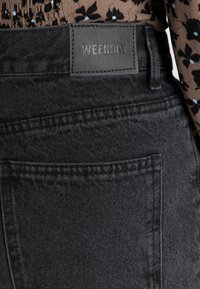 Mustan denimin farkut, joilla on teksturoitu pinta, hienovaraisia ommelainetta ja nahkalamina, jossa lukee "WEEKDAY", vyötäröllä.