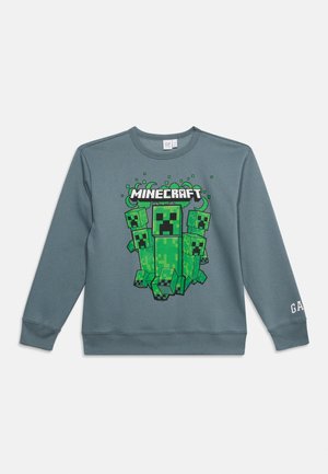 Sweat-shirt gris avec des personnages verts pixelisés de Minecraft Creeper et le texte « MINECRAFT » centré sur le devant, « GAP » sur la manche.