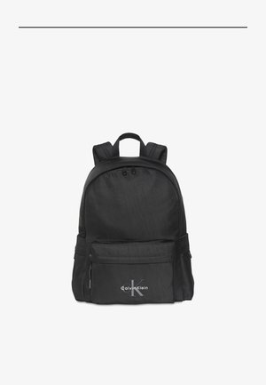 Zwarte Calvin Klein rugzak met voorvak met rits, verstelbare gevoerde schouderbanden en bovenste draaghandvat op een witte achtergrond.