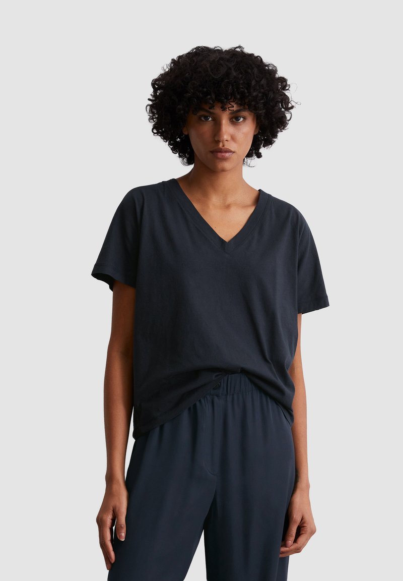 Black v-neck t-shirt made of cotton, featuring short sleeves and a relaxed fit, paired with dark, loose-fitting pants. Smooth texture.