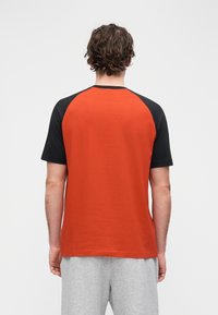 T-shirt de manga curta vermelha e preta com design raglan, feita de algodão, apresentando uma textura suave e blocos de cor sólida.