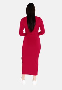 Czerwona midi sukienka z długim rękawem o slim fit, z bocznymi rozcięciami i prążkowaną fakturą. Noszona z białymi sneakersami dla uzyskania casualowego wyglądu.