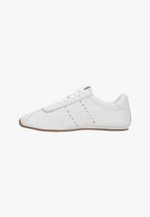 White leather sneaker with a curved toe, flat sole, and contrasting black stitching along the side. Smooth texture, simple lace-up design.