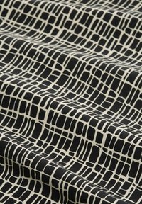 Tissu à motifs noir et blanc avec un design en grille, comportant des formes rectangulaires irrégulières sur un fond texturé.