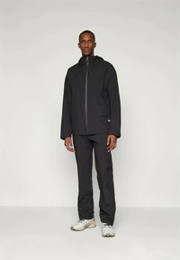 Veste imperméable noire avec col haut et fermeture éclair, accompagnée d'un pantalon assorti. Texture lisse avec des détails de design minimaux.