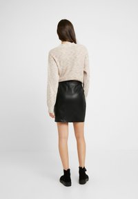 Knit sweater with multicolored specks and long sleeves, paired with a black leather mini skirt. Black ankle boots complete the look.