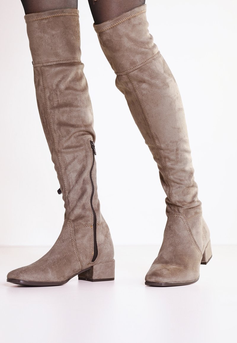 Beige Wildleder-Stiefel über das Knie mit runder Zehenpartie, niedrigem Blockabsatz und seitlichem Reißverschluss. Weiche Textur und taillierte Form.