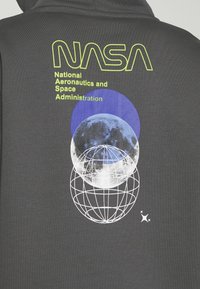 Sudadera gris con el logo de la NASA en un brillante amarillo, con un gráfico de la luna y el globo en azul y blanco, y acentos de estrellas.