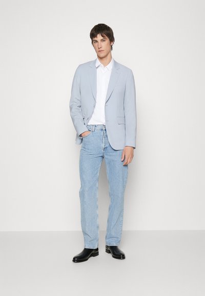 Lys blå blazer over en hvit skjorte, kombinert med lys blå jeans og svarte sko. Enkel design, tilpasset passform og glatt tekstur.