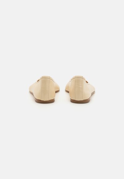 Chaussures slip-on en cuir beige avec une texture lisse, bout arrondi et semelle brune basse ; présentent un détail en découpe sur les côtés.