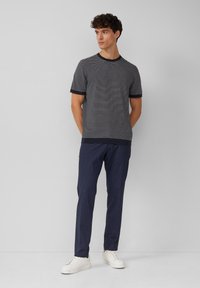 Pasiasty granatowy i biały t-shirt z okrągłym dekoltem i krótkimi rękawami, zestawiony z ciemnymi spodniami i białymi sneakersami. Prosty, nowoczesny design.