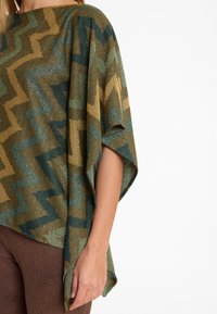 Poncho tricoté avec un motif zigzag dans des teintes de vert, or et marron ; présente une coupe ample, de larges manches et un matériau doux et texturé.