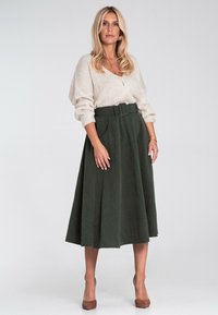 Sukienka robiona na drutach w kolorze kremowym z guzikami, połączona z ciemnozieloną spódnicą o wysokim stanie z paskiem i bocznymi kieszeniami. Całość dopełniają brązowe obcasy.