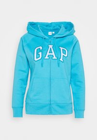 Turkusowa bluza z kapturem na zamek wykonana z miękkiego materiału. Z przodu białe litery "GAP" oraz dwie przednie kieszenie.