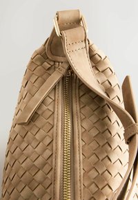 Beige geweven lederen tas met een gladde textuur, voorzien van een gouden rits en strap, verfraaid met een rechthoekige handgreepbevestiging.