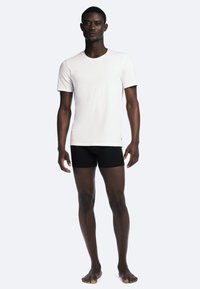 Hvid kortærmet t-shirt kombineret med sorte shorts, lavet af glat stof, med en klassisk rund halsudskæring og tætsiddende design.