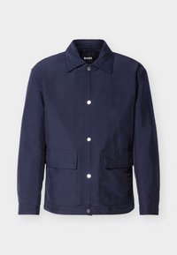 Ανδρικό μπουφάν σε ναυτικό μπλε χρώμα με κούμπωμα με κουμπιά, δύο μεγάλες τσέπες μπροστά και μυτερό γιακά, παρουσιάζεται πάνω σε λευκό φόντο.