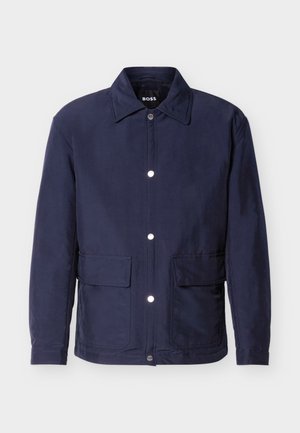 Ανδρικό μπουφάν σε ναυτικό μπλε χρώμα με κούμπωμα με κουμπιά, δύο μεγάλες τσέπες μπροστά και μυτερό γιακά, παρουσιάζεται πάνω σε λευκό φόντο.