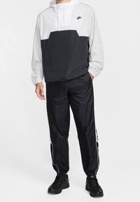 Czarna i biała kurtka przeciwwiatrowa Nike z elastycznymi mankietami i półzamkiem, zestawiona z czarnymi spodniami dresowymi z białymi wstawkami po bokach.