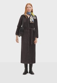 Lungo vestito grigio scuro con colletto, chiusura con bottoni e vita con cintura. Abbinato a stivali neri fino al ginocchio e a una sciarpa con motivo. Borsa nera indossata a tracolla.
