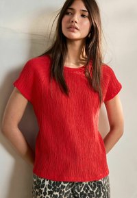 Haut court à manches courtes texturé rouge avec un col rond, associé à un pantalon à imprimé léopard, offrant une coupe décontractée et des détails subtils.
