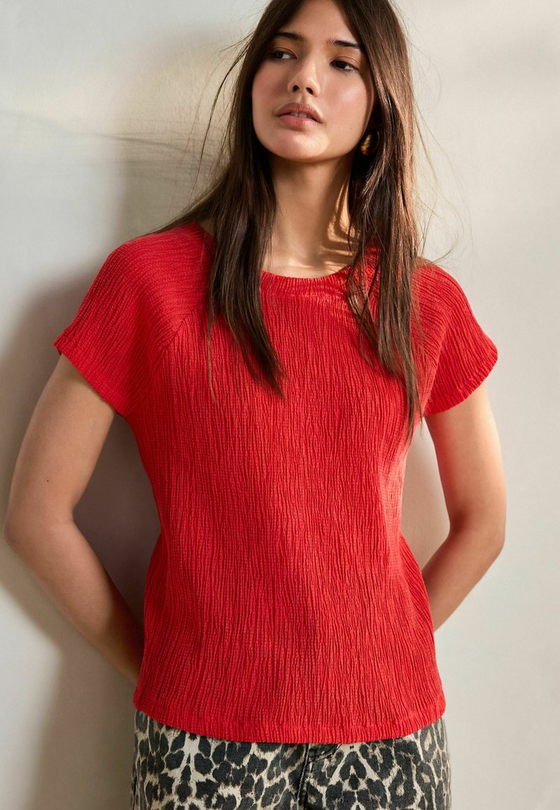 Haut court à manches courtes texturé rouge avec un col rond, associé à un pantalon à imprimé léopard, offrant une coupe décontractée et des détails subtils.