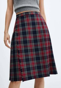 Jupe à carreaux avec un motif bleu marine, rouge et vert, dotée d'un ourlet effiloché et d'une fente latérale. Fabriquée en tissu texturé. Coupe évasée.