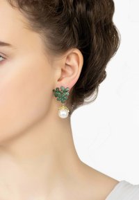 Zöld kőből készült virágmintás fülbevalók nagy gyöngy cseppel, arany díszítéssel és részletes kialakítással. Szögletes és levél formák prominens elhelyezésével.