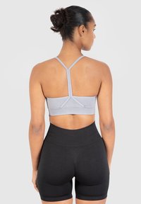 Lichtgrijze sportbeha met racerback ontwerp, textuurmateriaal en elastische band, gecombineerd met hoge zwarte shorts. Achteraanzicht.