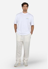 Camiseta blanca de algodón con logo "PEGADOR" en azul; pantalones de lino beige con textura ligera; zapatillas grises con acentos azules.