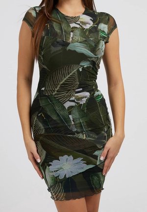 Femme portant une robe ajustée à manches courtes avec un motif de feuilles tropicales et de fleurs vertes et noires.