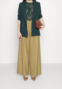 Groene blazer over een zwarte kanttop, brede khaki broek en een bruin clutch. Accessoires zijn een groene ring en slangenprint hakken.