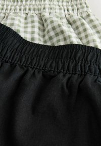 Deux ceintures froncées, une en tissu noir uni et une en tissu à carreaux verts et blancs, montrées en gros plan.