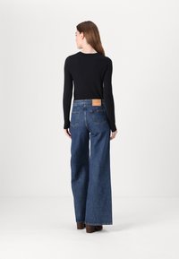 Svart långärmad topp som är kombinerad med vida blå jeans av denim. Jeansen har en tag i beige läder vid midjan och bakfickorna.