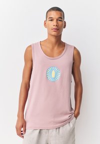 Gaiši rozā bez Piedurknēm kokvilnas topiņš ar apaļu grafisku dizainu centrā, kas papildināts ar dzeltenām un zilām krāsām. Gluda tekstūra.