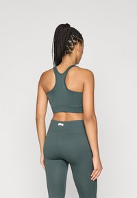 Πράσινο ριγέ αθλητικό σουτιέν με σχέδιο racerback, συνδυασμένο με αντίστοιχες ψηλόμεσες κολάν που διαθέτουν μια διακριτική ετικέτα branding στη ζώνη.