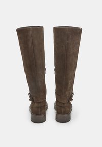 Stivali al ginocchio in suede marrone con un design leggermente sformato, cuciture a contrasto e cinghie alla caviglia. La suola è testurizzata per garantire aderenza.