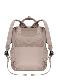 Zaino beige realizzato in tessuto resistente, dotato di spallacci imbottiti, maniglia superiore, tasche esterne laterali e un accento testurizzato su un lato.