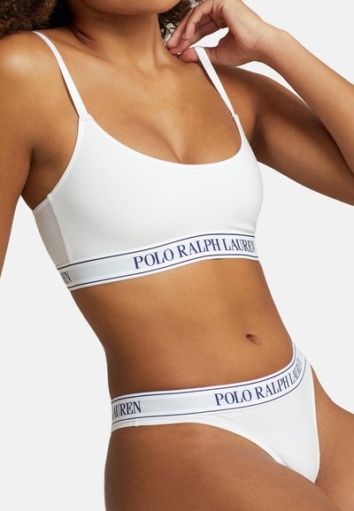 Balts ribots krūšturis ar plānām siksnām un plašu joslu, kurā ir uzraksts "POLO RALPH LAUREN" tumši zilā krāsā. Kopā ar atbilstošām balta ribota apakšveļas biksēm.