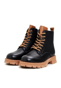 Bottes chevilles en cuir noir avec accents marron, présentant un design à lacets, une semelle épaisse en caoutchouc, et une finition texturée sur la tige.