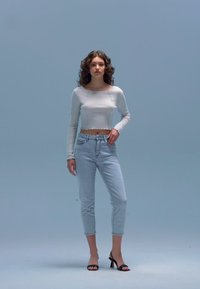 Bílý crop top s dlouhým rukávem a třepeným lemem; světle modré džínové kalhoty s vysokým pasem; černé sandály na podpatku s otevřenou špičkou.