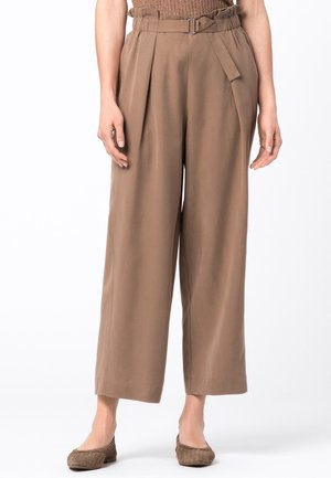 Brązowe spodnie z wysokim stanem i szerokimi nogawkami, zapinane na materiałowy pasek i plisowane, noszone z brązowymi, teksturowanymi balerinami, widoczne od talii do stóp.