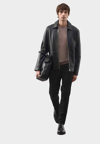 Veste en cuir noire avec fermeture éclair, haut marron, pantalon noir et chaussures noires. Le mannequin porte un sac noir. Design simple et moderne.