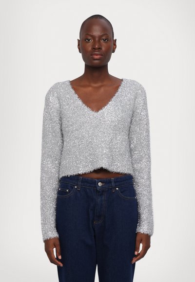 Pull court en tricot argenté et duveteux avec un décolleté en V et des manches longues, associé à un jean en denim bleu foncé avec un bouton et des poches.